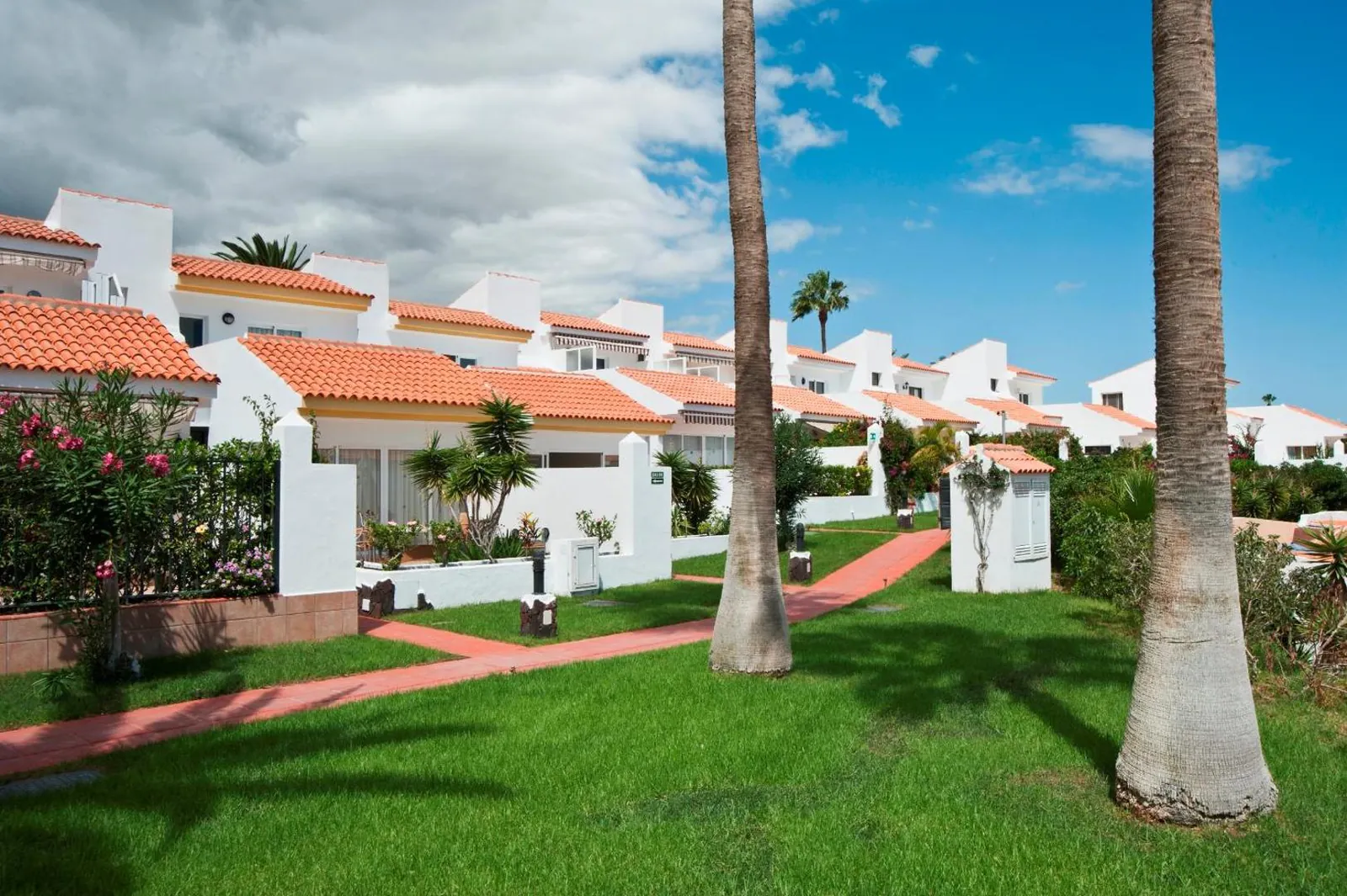 White two-storey villas with red roofs around a lawn with palms